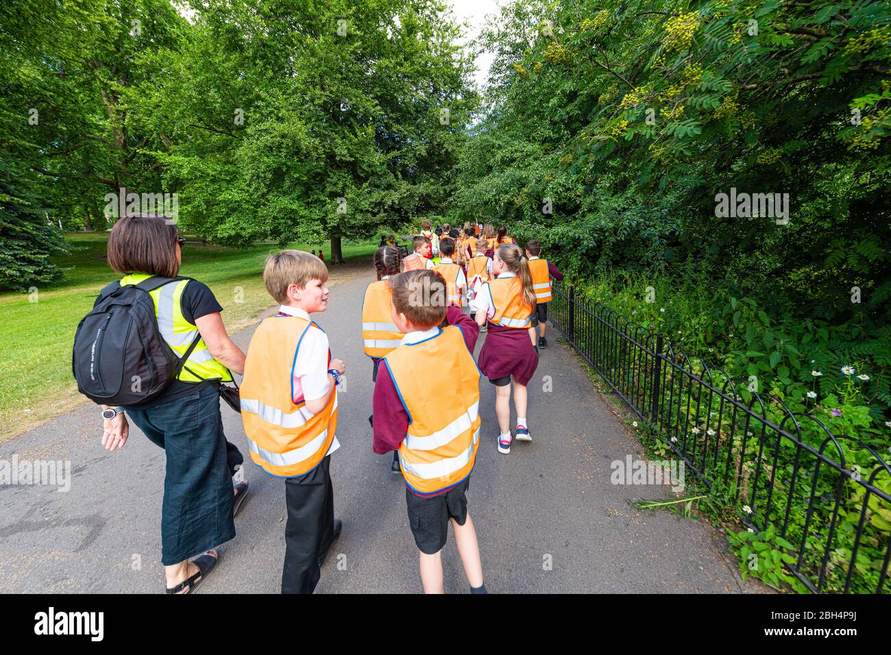 London, UK - June 21, 2018: St James Park green summer with many crowd of people school children walking on sidewalk road on field trip in vests Stock Photo