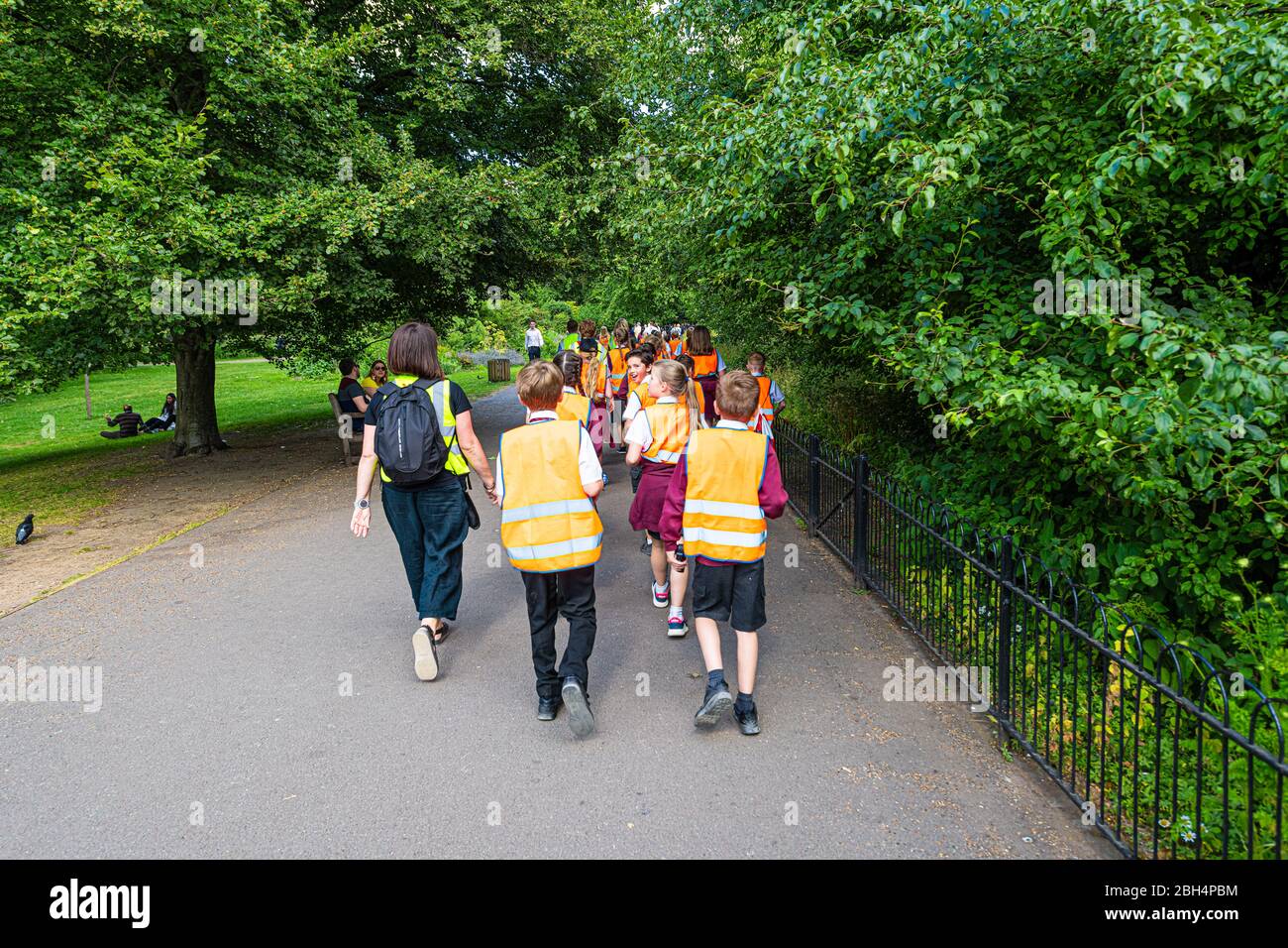 London, UK - June 21, 2018: St James Park green summer with many people school children walking on sidewalk road on field trip in vests Stock Photo