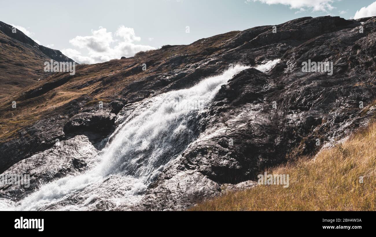 Sunny white scenic norwegian powerful river cascade waterfall with dark rocks, color graded. Nature travel clean falling water landscape Stock Photo
