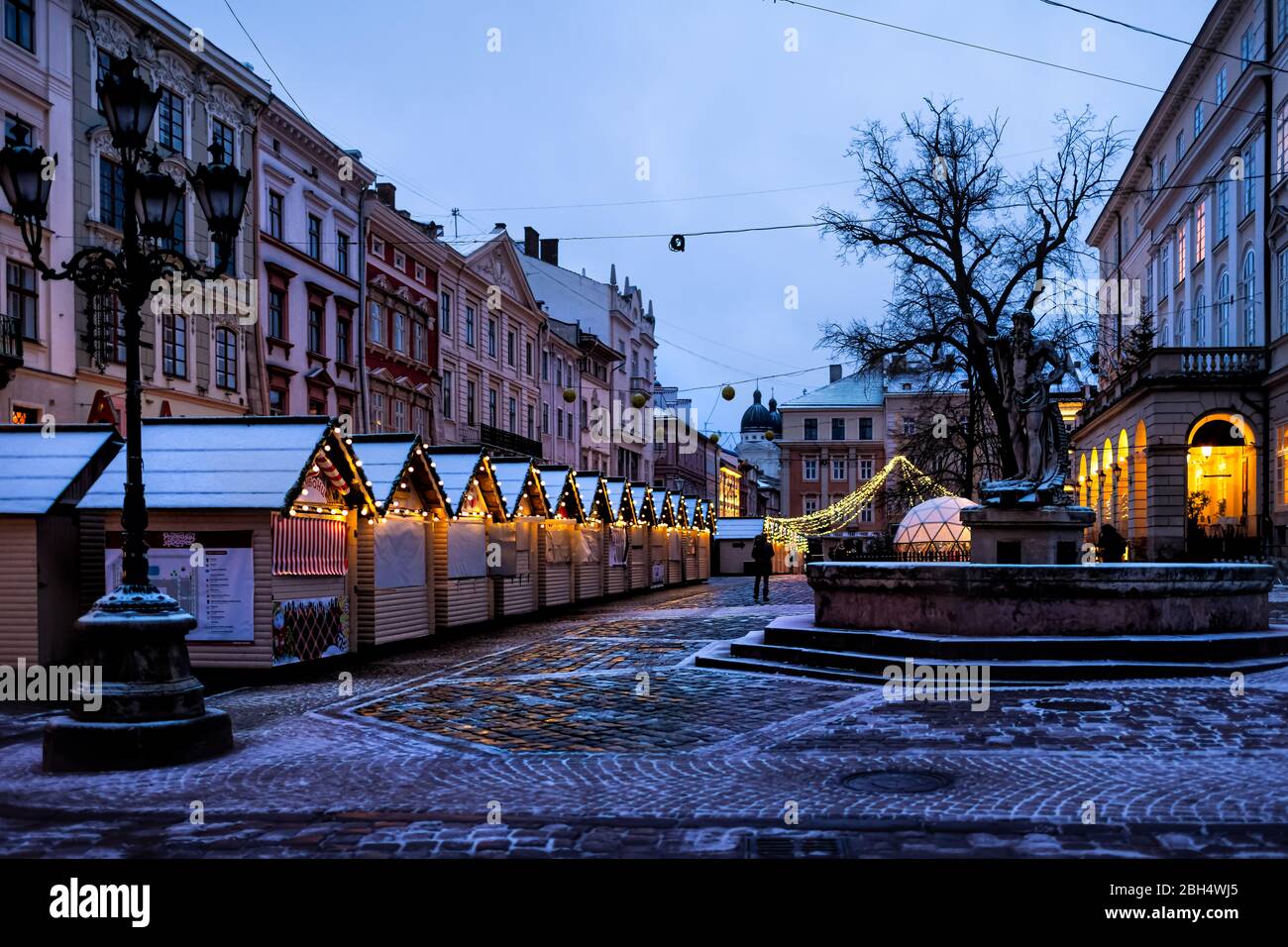 Lviv, Ukraine - December 28, 2019: Old town market square water fountain in Lvov with winter Christmas illumination and empty rynok at night with snow Stock Photo
