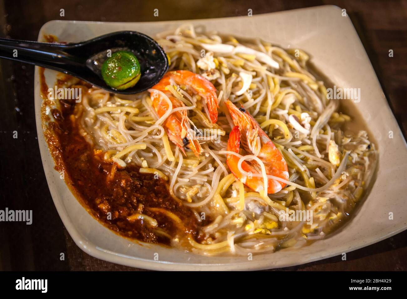 Singapore cuisine Seafood Hokkien Mee with jumbo prawns, squid, pork and eggs fried together with yellow noodles and vermicelli in seafood broth. Serv Stock Photo