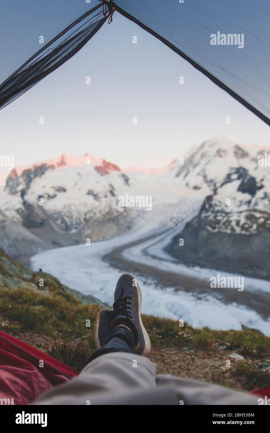 Man lying inside tent with Gorner Glacier in distance in Valais, Switzerland Stock Photo