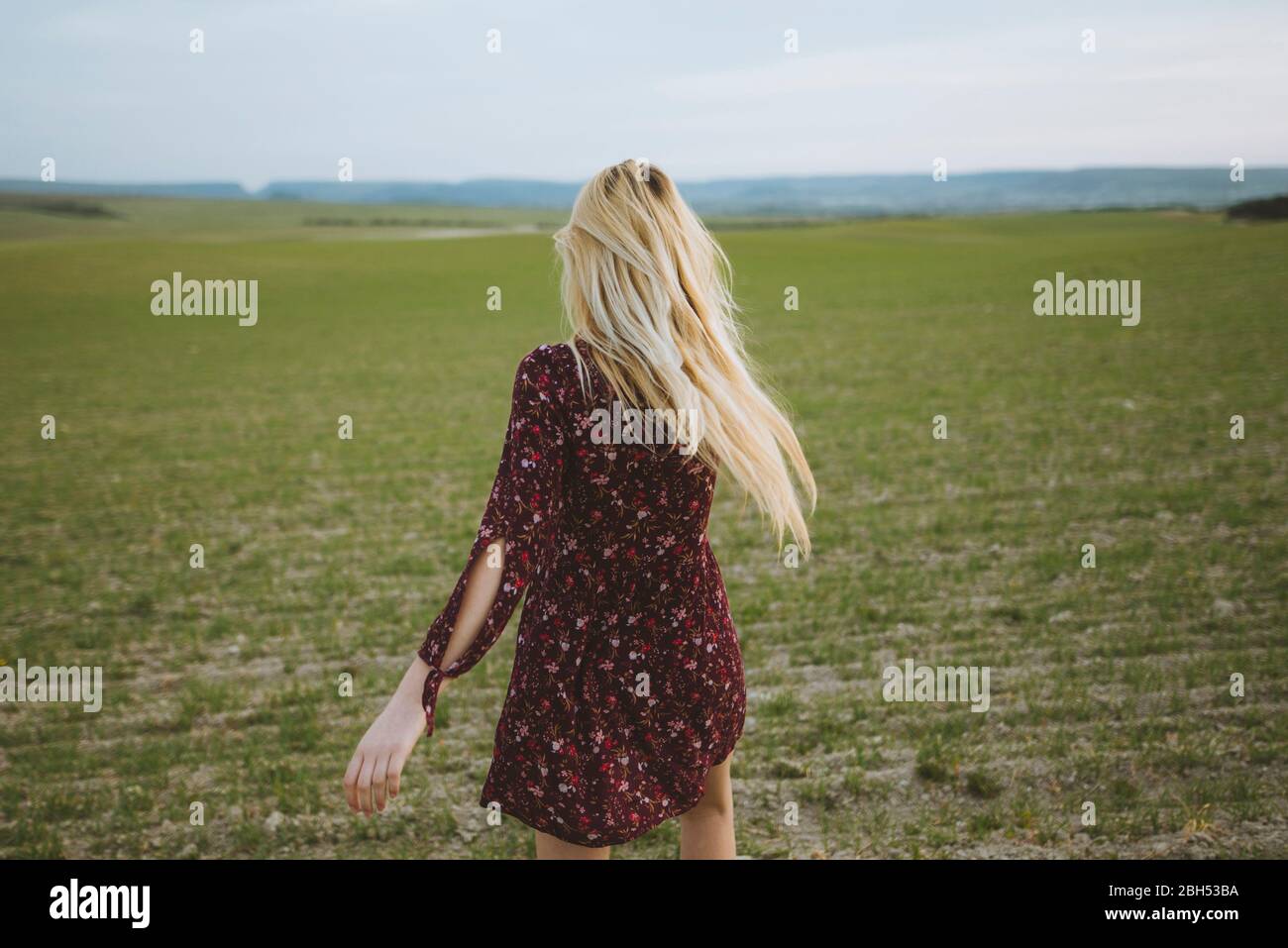 Young Caucasian blonde woman in dress running in spring field at sunset Stock Photo