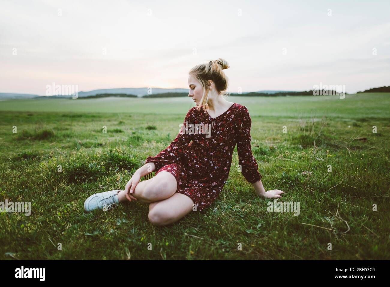 Blonde woman wearing dress sitting in field Stock Photo