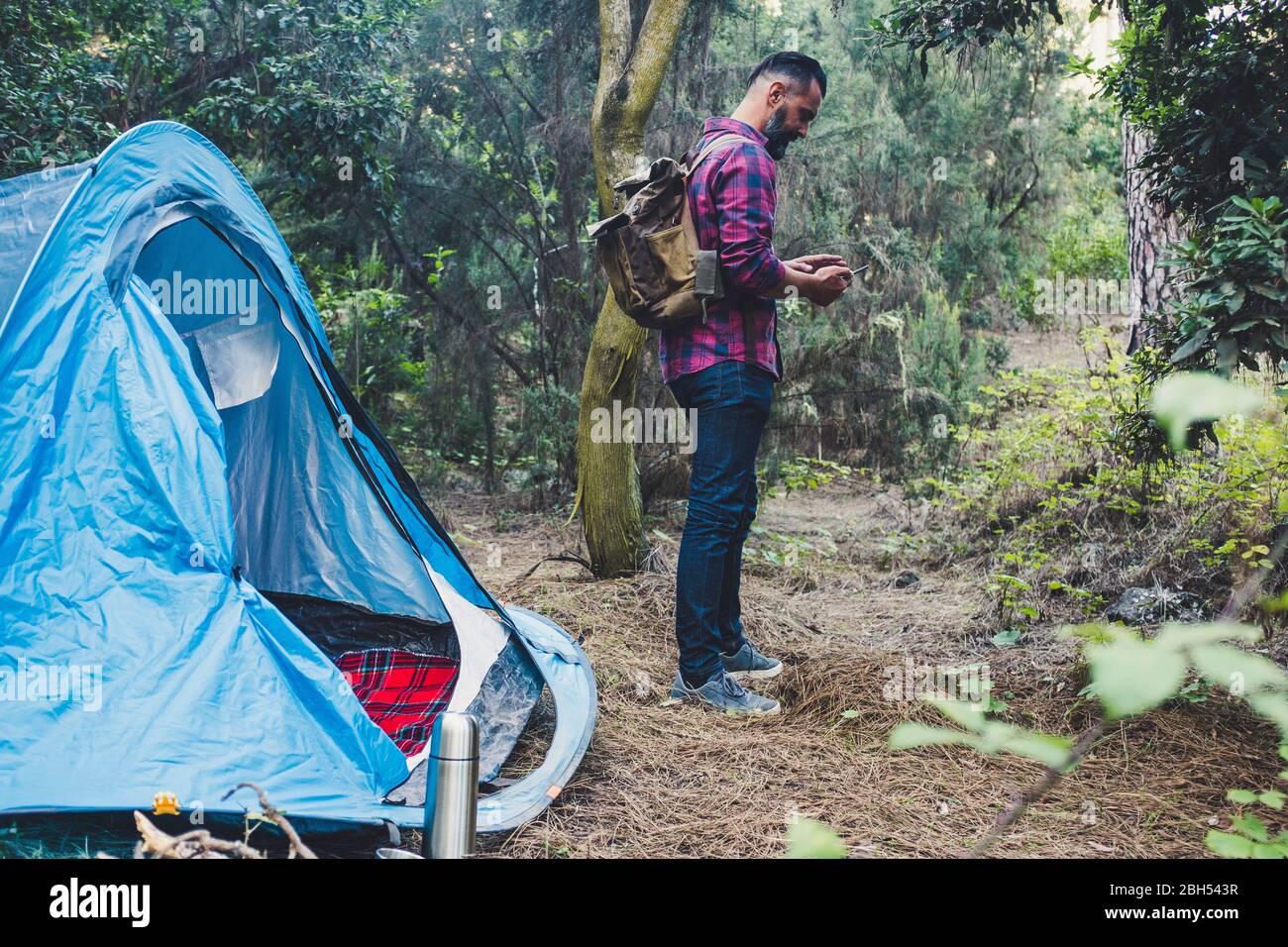 Man using smart phone by tent in forest Stock Photo