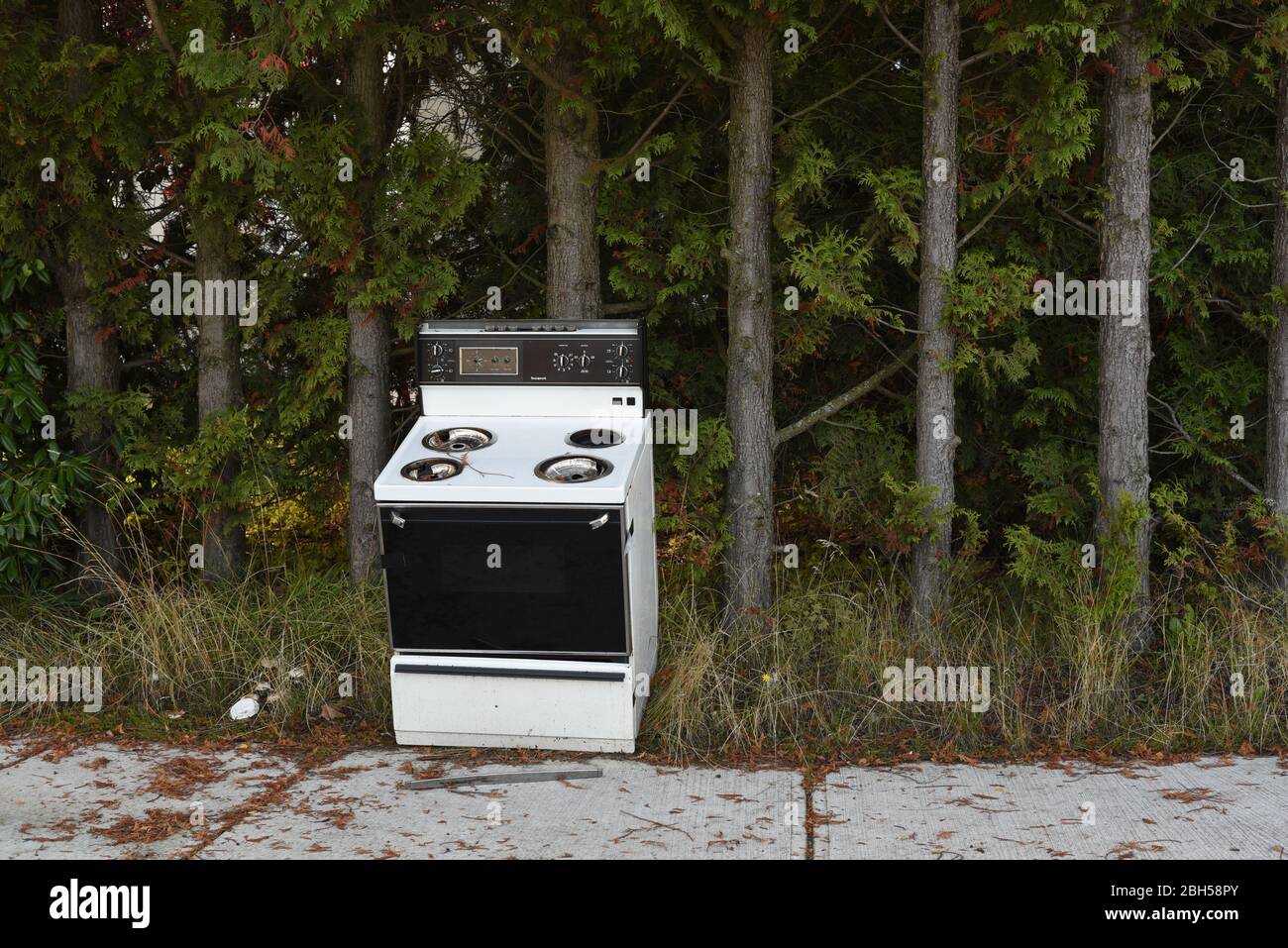 An abandoned old stove and oven is abandoned on a sidewalk in front of a row of trees in Victoria, British Columbia, Canada Stock Photo