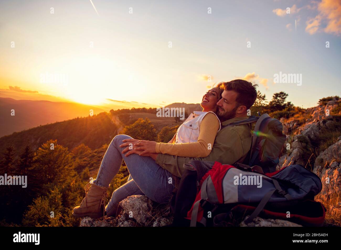 Couple Man and Woman sitting on cliff enjoying mountains and clouds ...