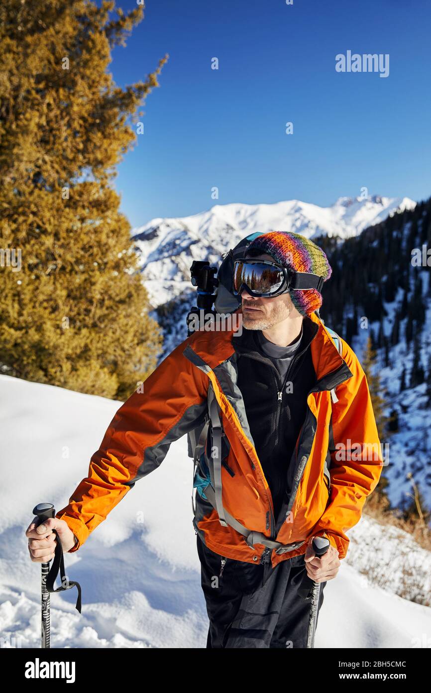 Portrait of skier in orange jacket and mask at snow mountain background at sunny day Stock Photo