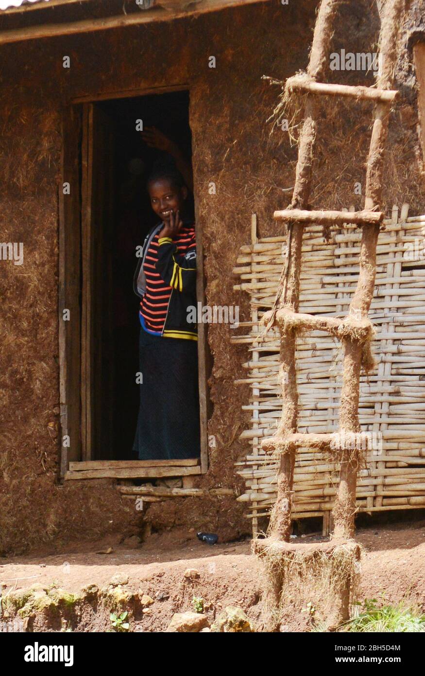 An Ethiopian woman standing at her village home doorstep and smiling. Stock Photo
