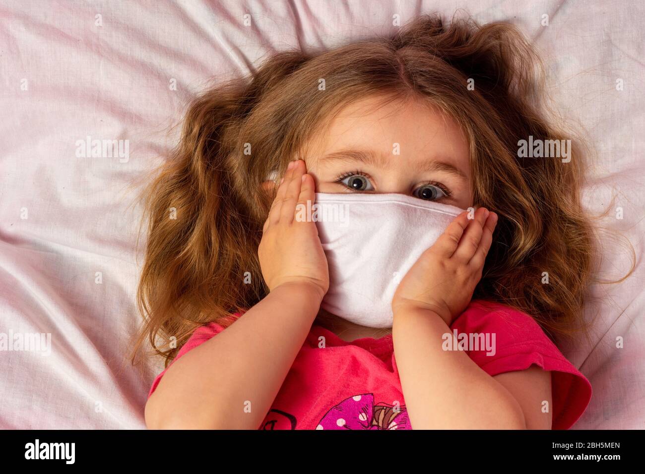 Little girl with dark hair lying on bed in medical mask and holding ...