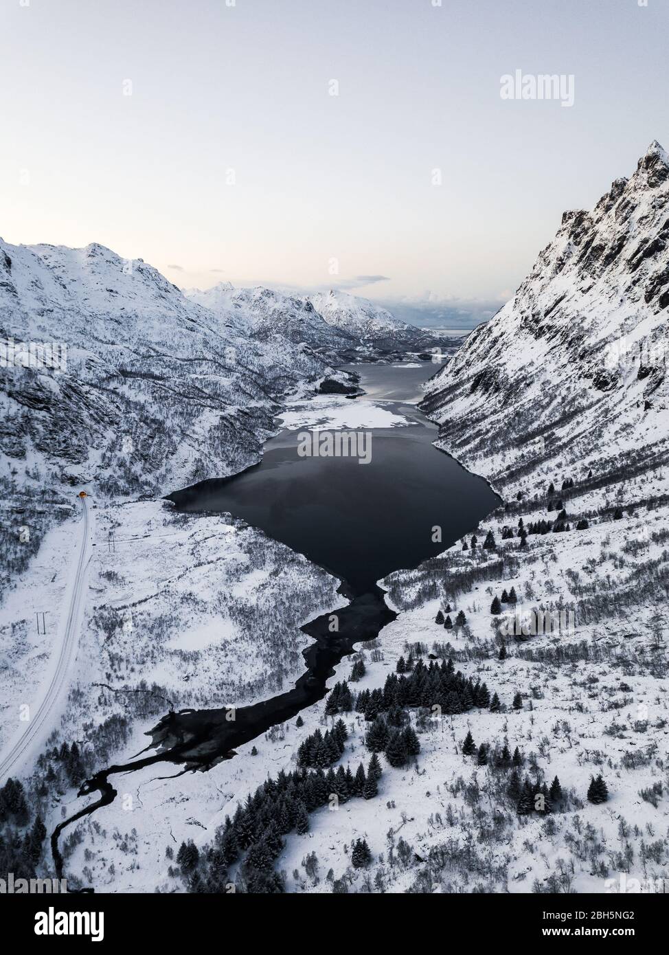 Aerial drone photo of a valley in lofoten. in the middle there is a sea with mountains on the side, the mountains are covered in snow Stock Photo