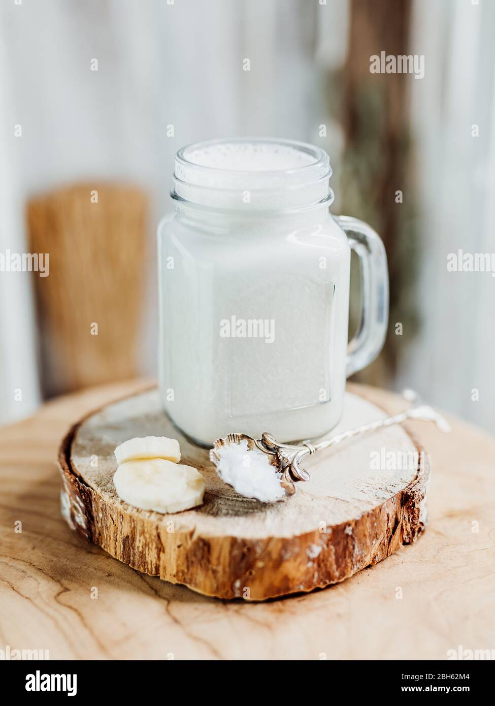Healthy protein shake with banana, salt in a stylish glass, decorated with a banana slice and le fleur salt on a wooden plate, white, yellow, beige Stock Photo