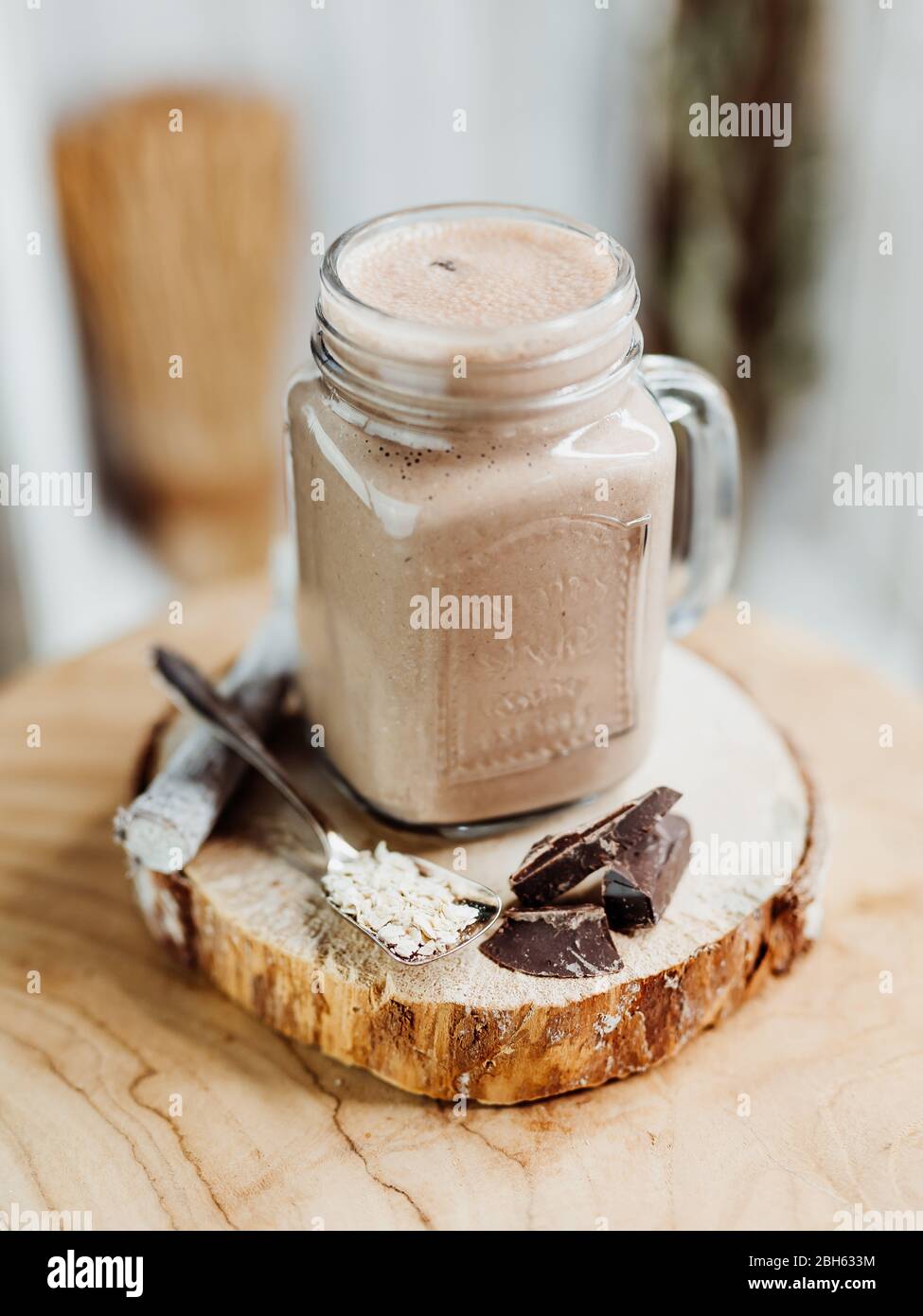Healthy protein shake with banana, peanut butter, oats and agave syrup in a stylish glass, decorated with chocolate protein, oatmeal and mint Stock Photo