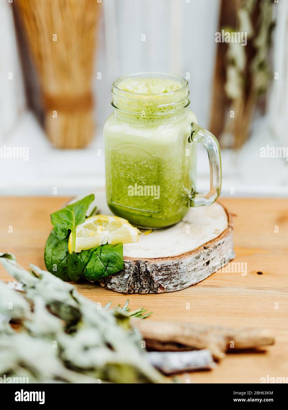 Healthy vitamin shake with spinach, ginger and almond milk in a stylish glass, decorated with lemon and spinach leaf on a wooden plate, green, yellow Stock Photo