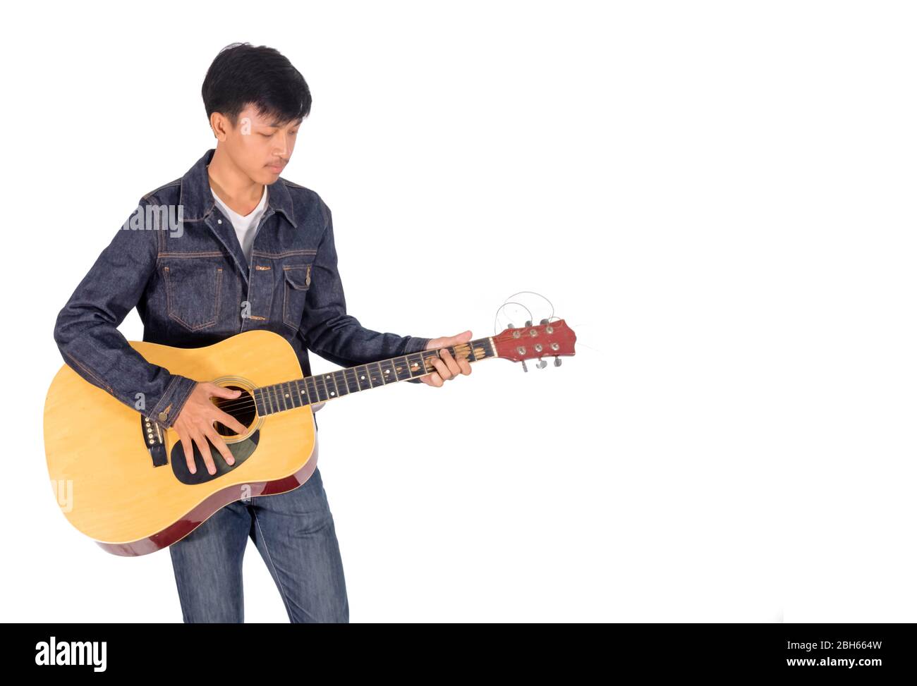 A portrait of an Asian man in blue jeans jacket is playing an old guitar copy space. Stock Photo