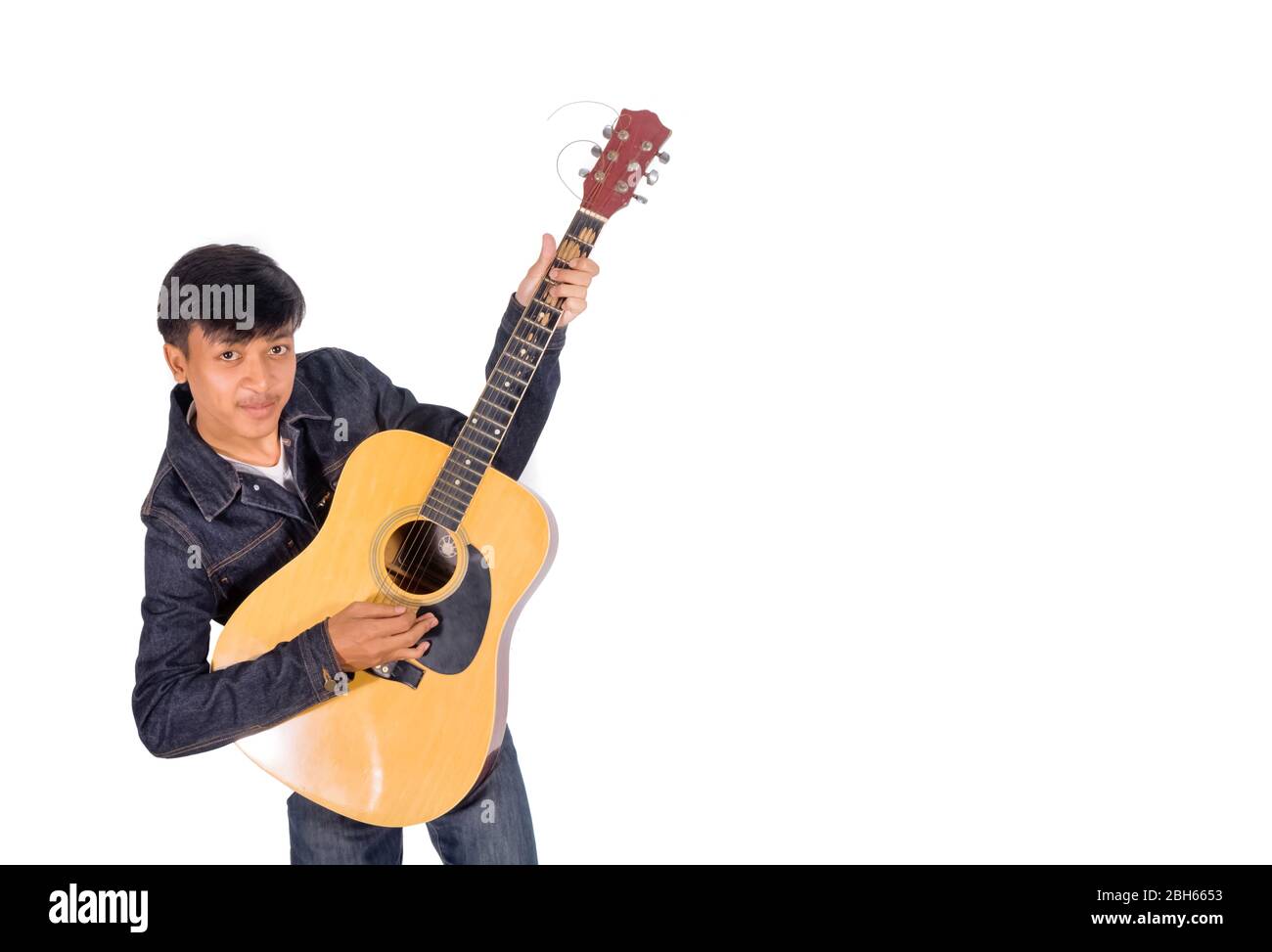 A portrait of an Asian man in blue jeans jacket is playing an old guitar copy space. Stock Photo