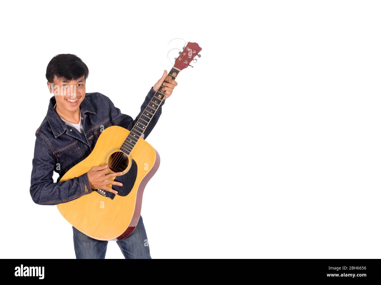 A portrait of an Asian man in blue jeans jacket is playing an old guitar copy space. Stock Photo