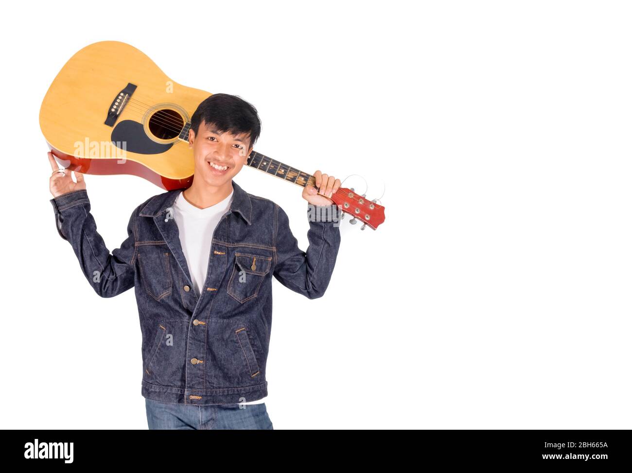 A portrait of an Asian man in blue jeans jacket is bearing an old guitar copy space. Stock Photo