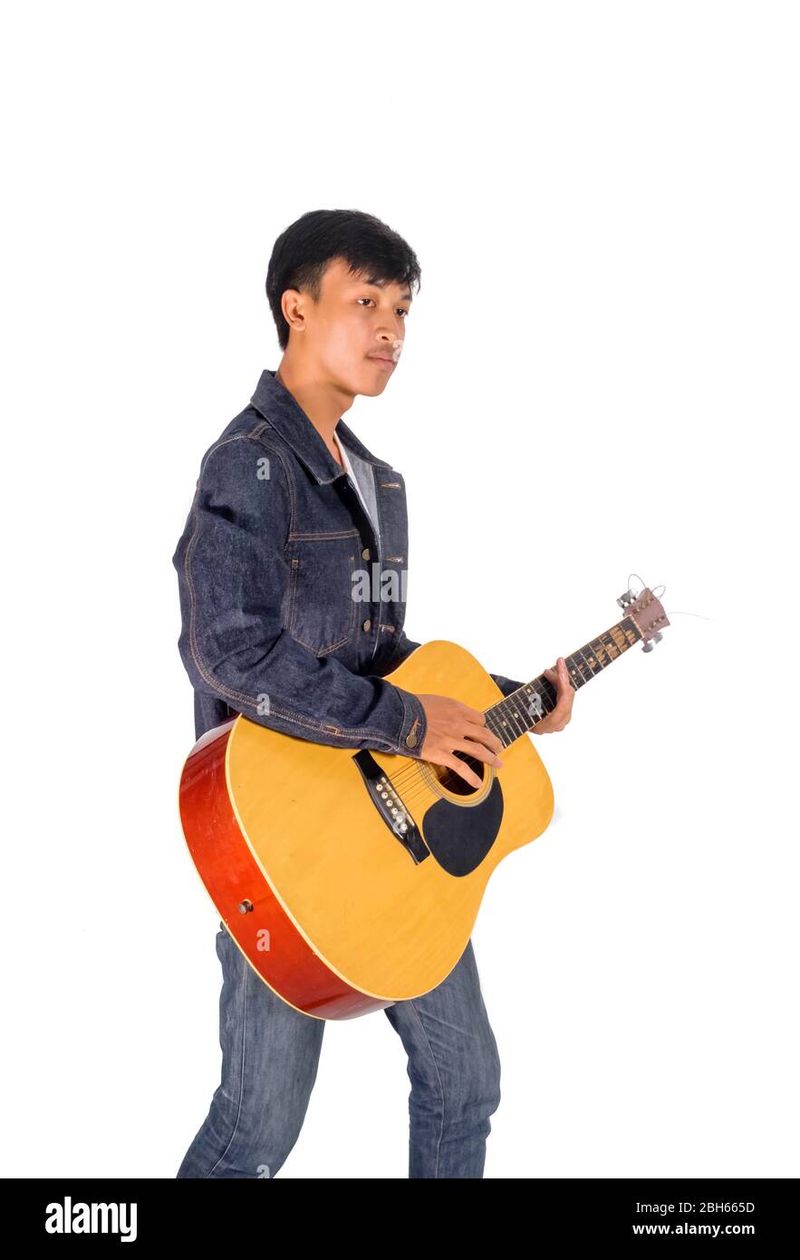 A portrait of an Asian man in blue jeans jacket is playing an old guitar copy space. Stock Photo