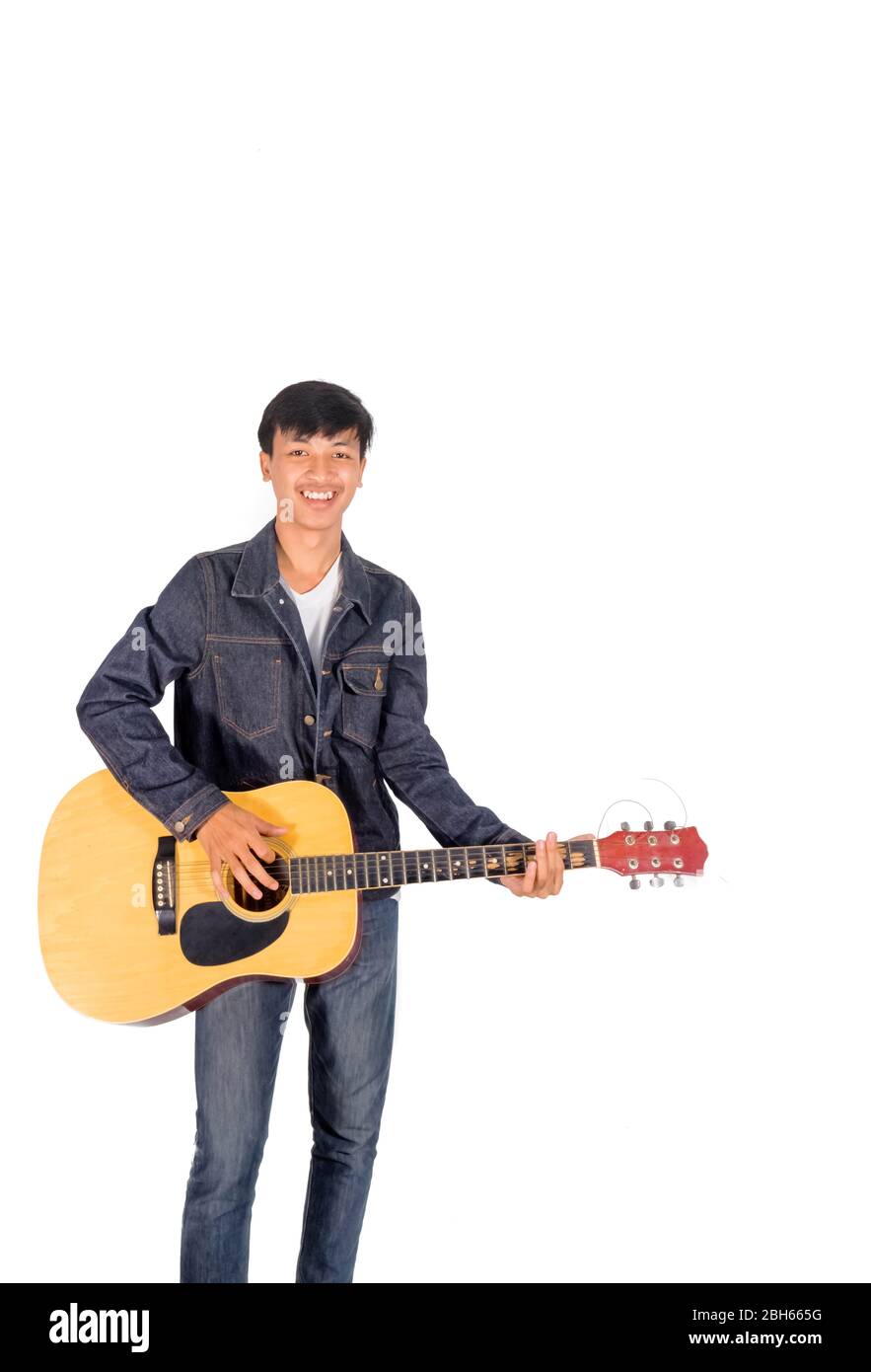 A portrait of an Asian man in blue jeans jacket is playing an old guitar copy space. Stock Photo