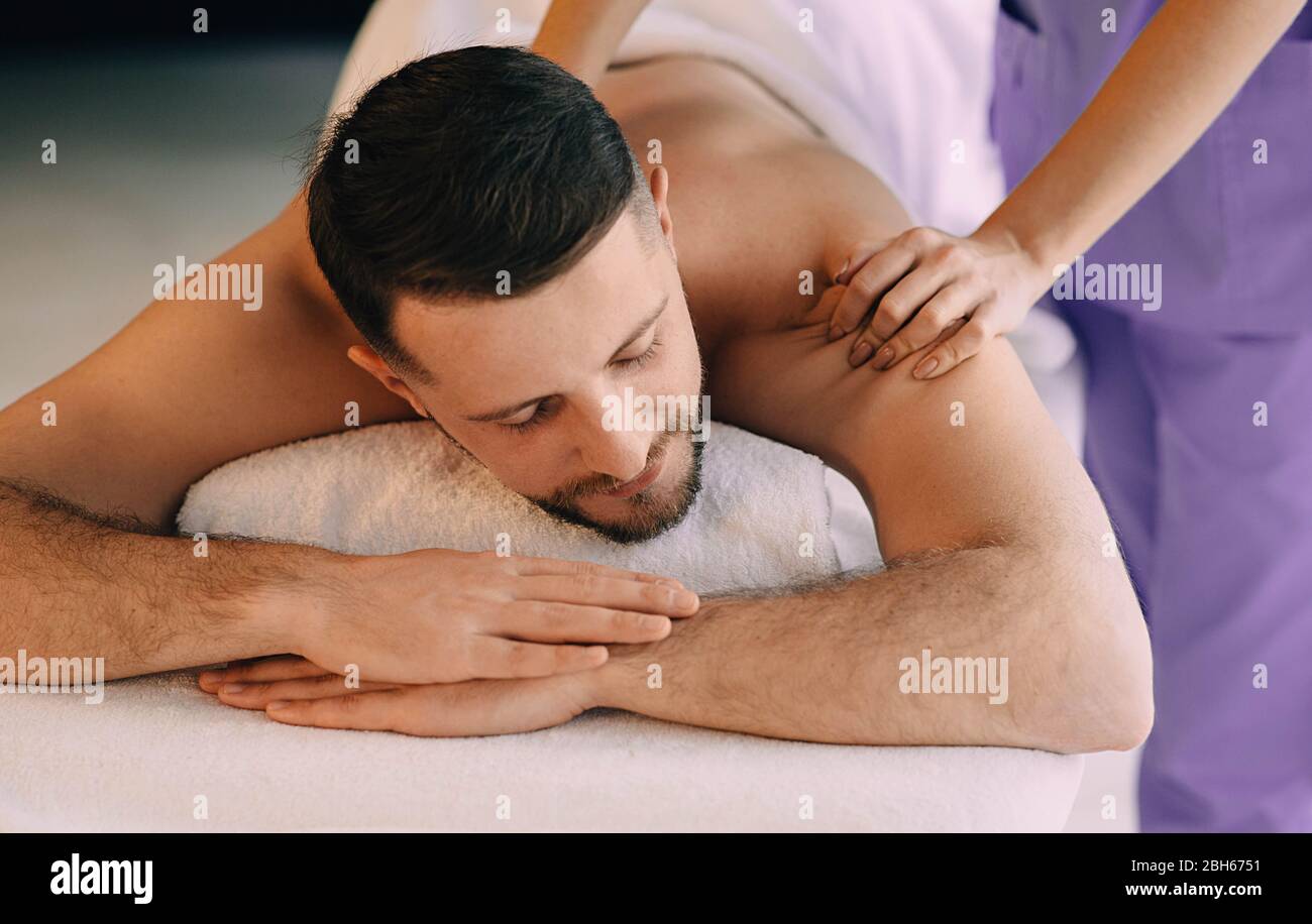 Brunette man relaxing in the spa while getting back massage. Stock Photo
