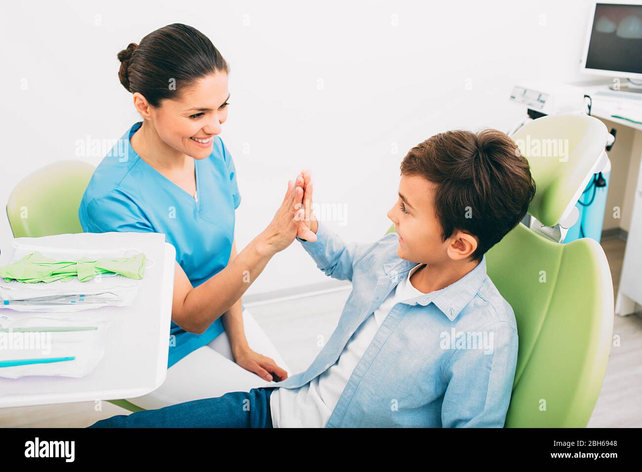 Happy little boy having five with his dentist . He sitting at dental chair, after teeth treatment. Pediatric dentistry Stock Photo