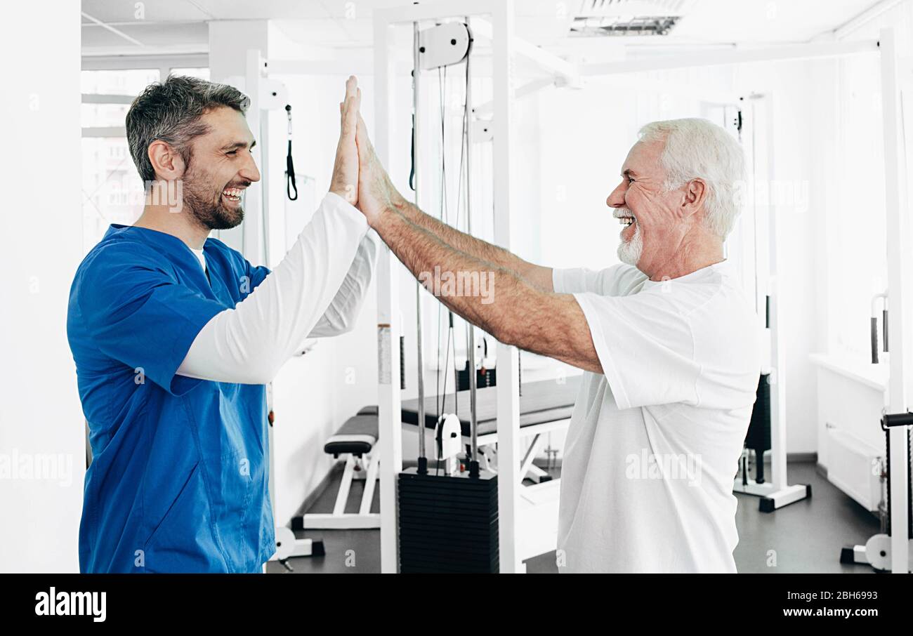 Senior man and Physical Therapist have five after successful physio treatment. physio rehabilitation Stock Photo