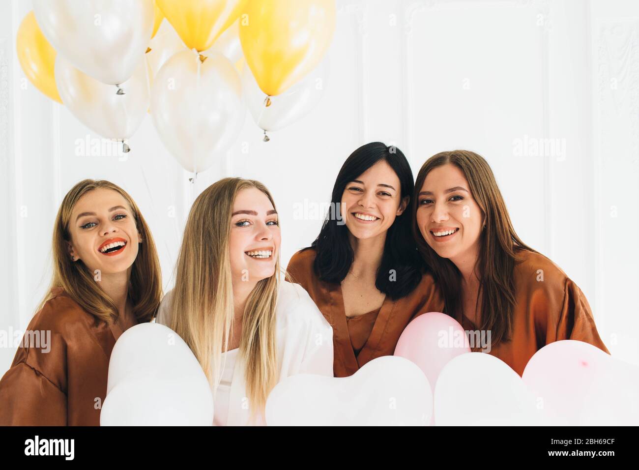 Beautiful woman wearing satin robes celebrating bachelorette, holding balloons. Woman with her friends have a cool party Stock Photo
