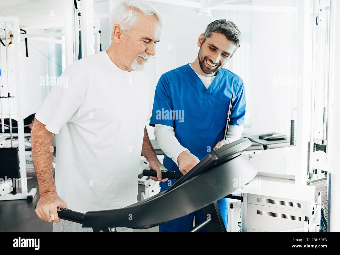 Senior patient having physical therapy with his therapist at hospital. Elderly man training on a treadmill. Stock Photo
