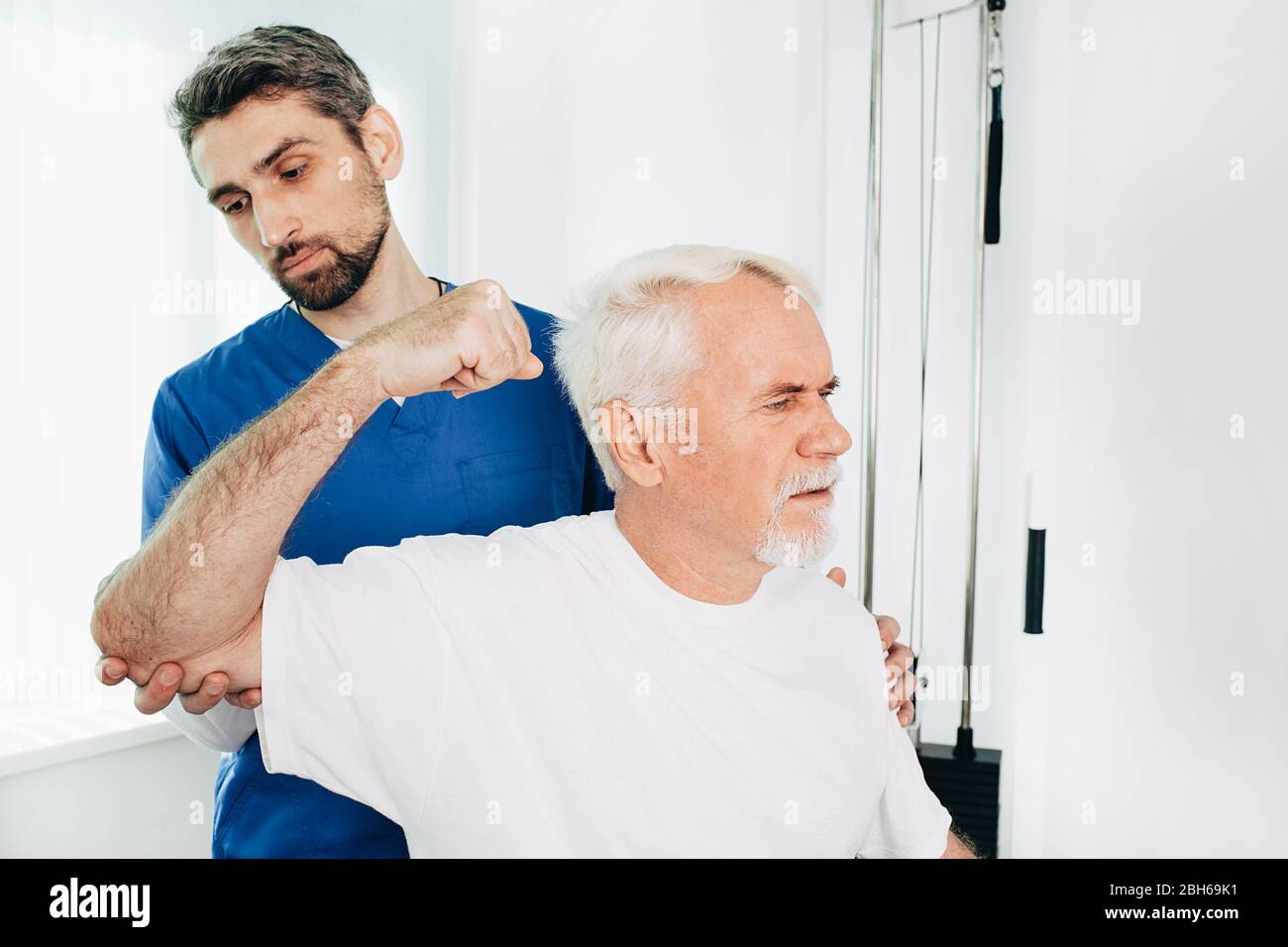 Male physical therapist holding senior patient while he stretches his cubit. Physio rehab at wellness center Stock Photo