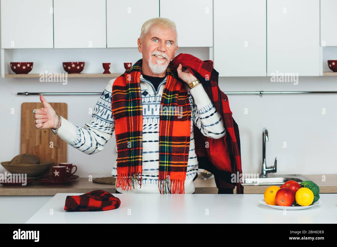 elderly man showing thumbs up, smiling looking at the camera and standing at home in his white kitchen. happy seniors people at home Stock Photo