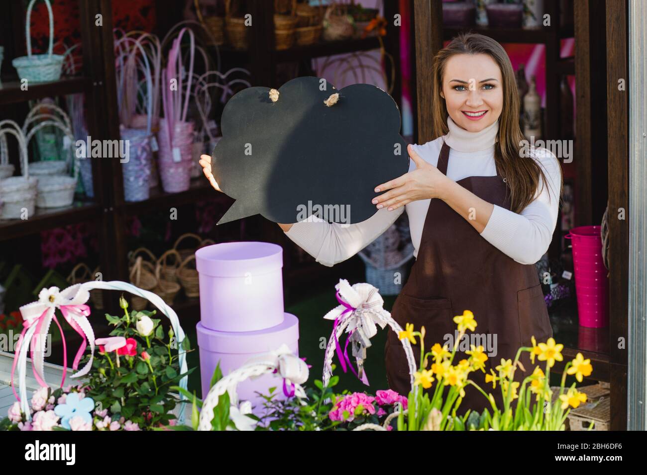 Attractive flower seller holding empty speech bubbles and looking at camera standing at floral store Stock Photo