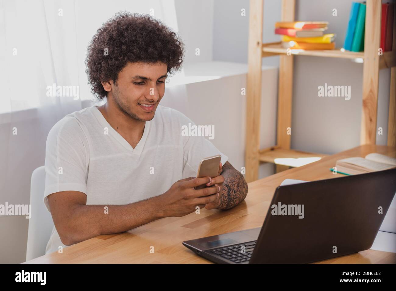 Pleasant chat . Attractive man mulatto with curly hair, holding smart phone and write a message with with positive emotions while sitting at his worki Stock Photo