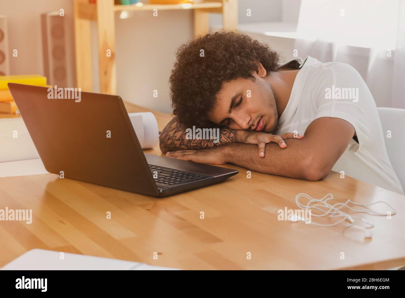 tired man leaned elbows on the table and closed eyes, while working at the computer. On the desk is a laptop and other tools for office working Stock Photo