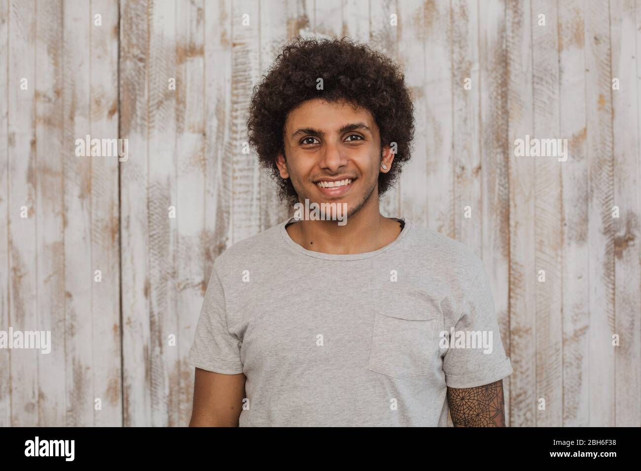 Mulatto with a perfect smile. Portrait cheerful curly haired man looking at the camera, while standing against old wooden background Stock Photo