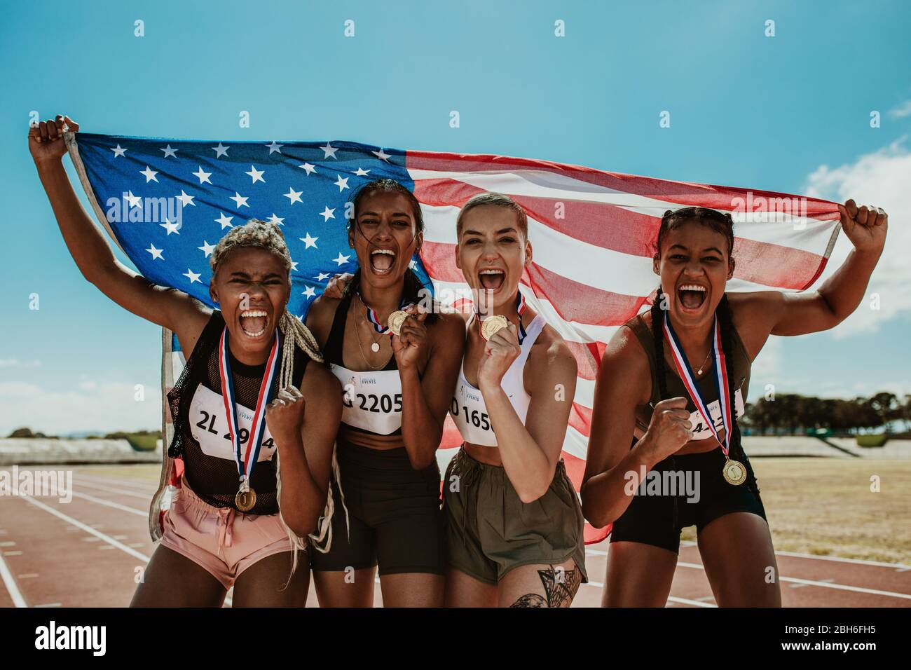 Group of female runner with medals winning a competition. American women athletes celebrating victory while standing together on racetrack holding the Stock Photo