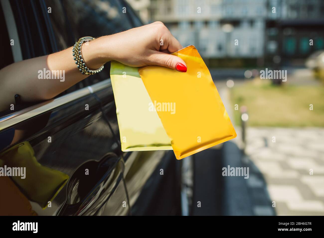 female hand holding blank foil food doypack from the car window Stock Photo