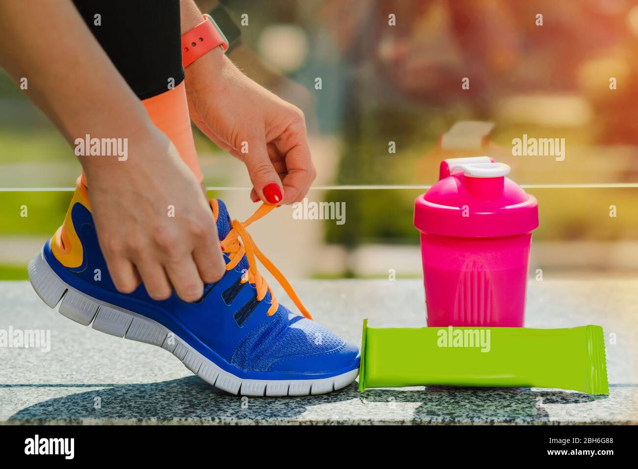 woman getting ready for fitness workout outdoors, lacing running shoes near sports nutrition. sports training on a sunny day Stock Photo