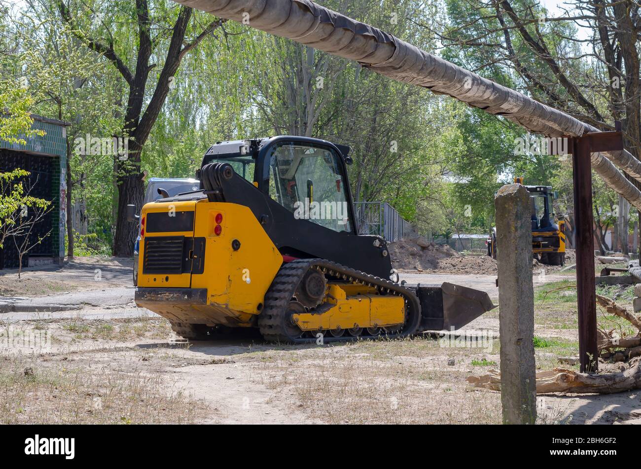 Small crawler excavator with rubber tracks. Yellow skid steer loader at