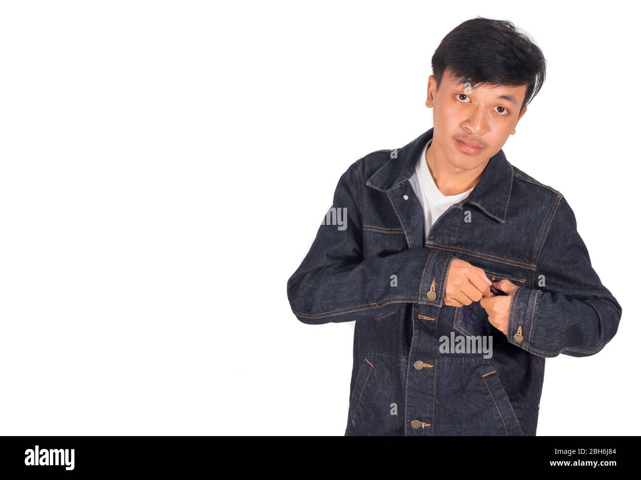 An Asian boy puts on too big jeans jacket white background. Stock Photo