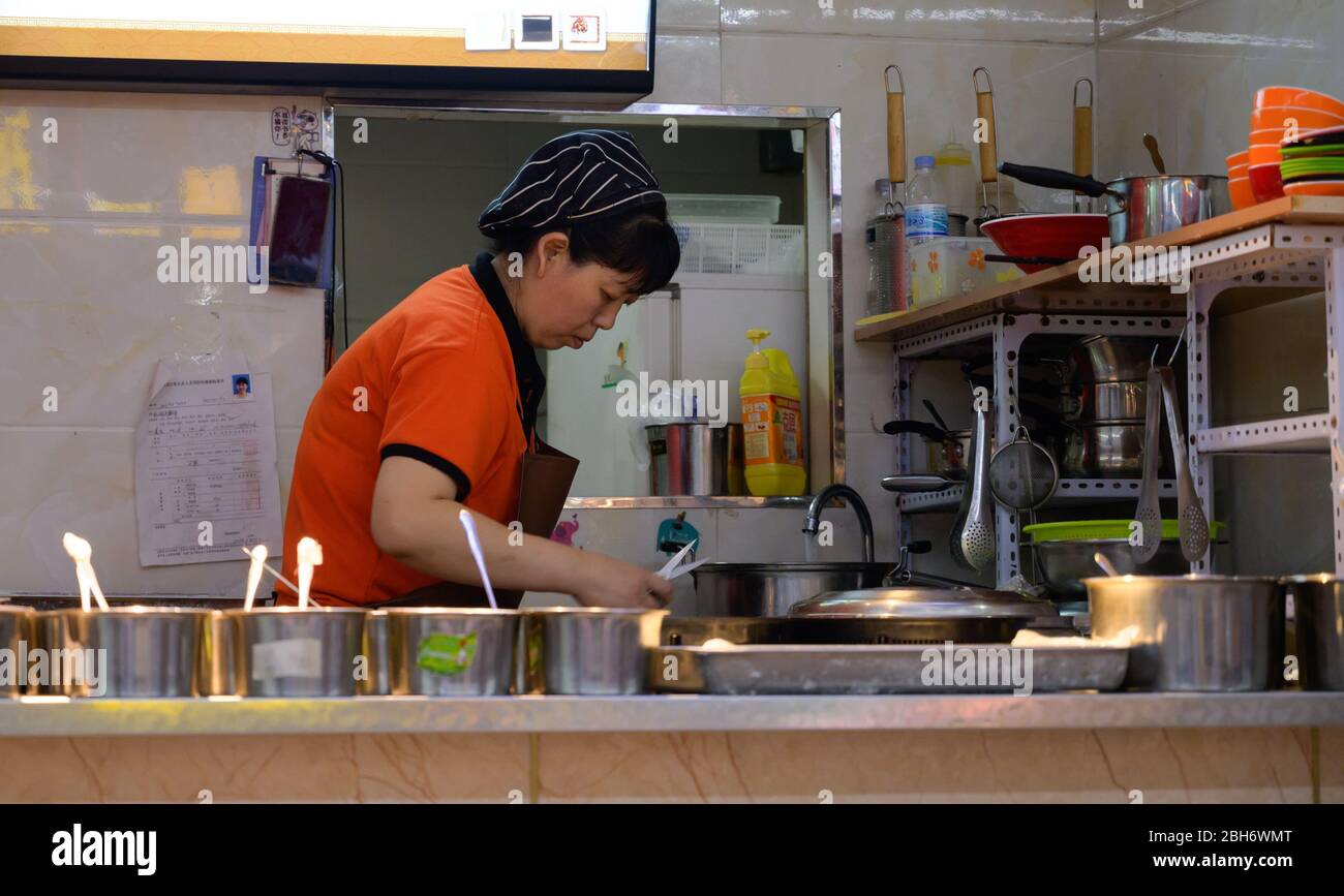 MISHAN, CHINA - JULY 28, 2019: Asian elderly woman cooking food on the kitchen in a fast food cafe. Stock Photo