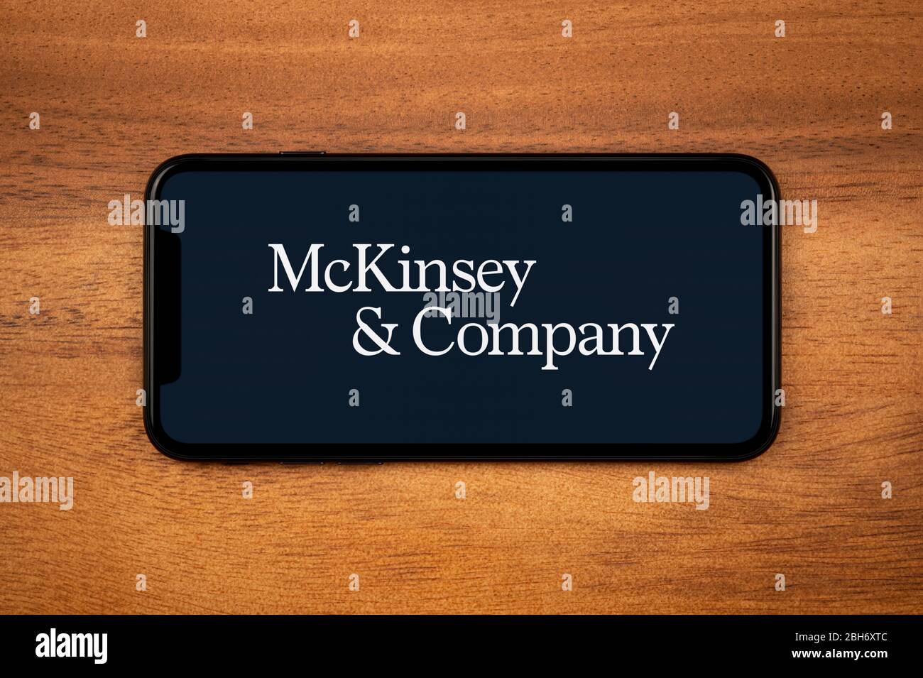 A smartphone showing the McKinsey & Company logo rests on a plain wooden table (Editorial use only). Stock Photo