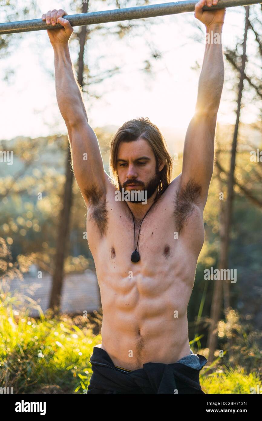 Young bearded man doing pull ups in the park with beautiful sunset on the mountain Stock Photo