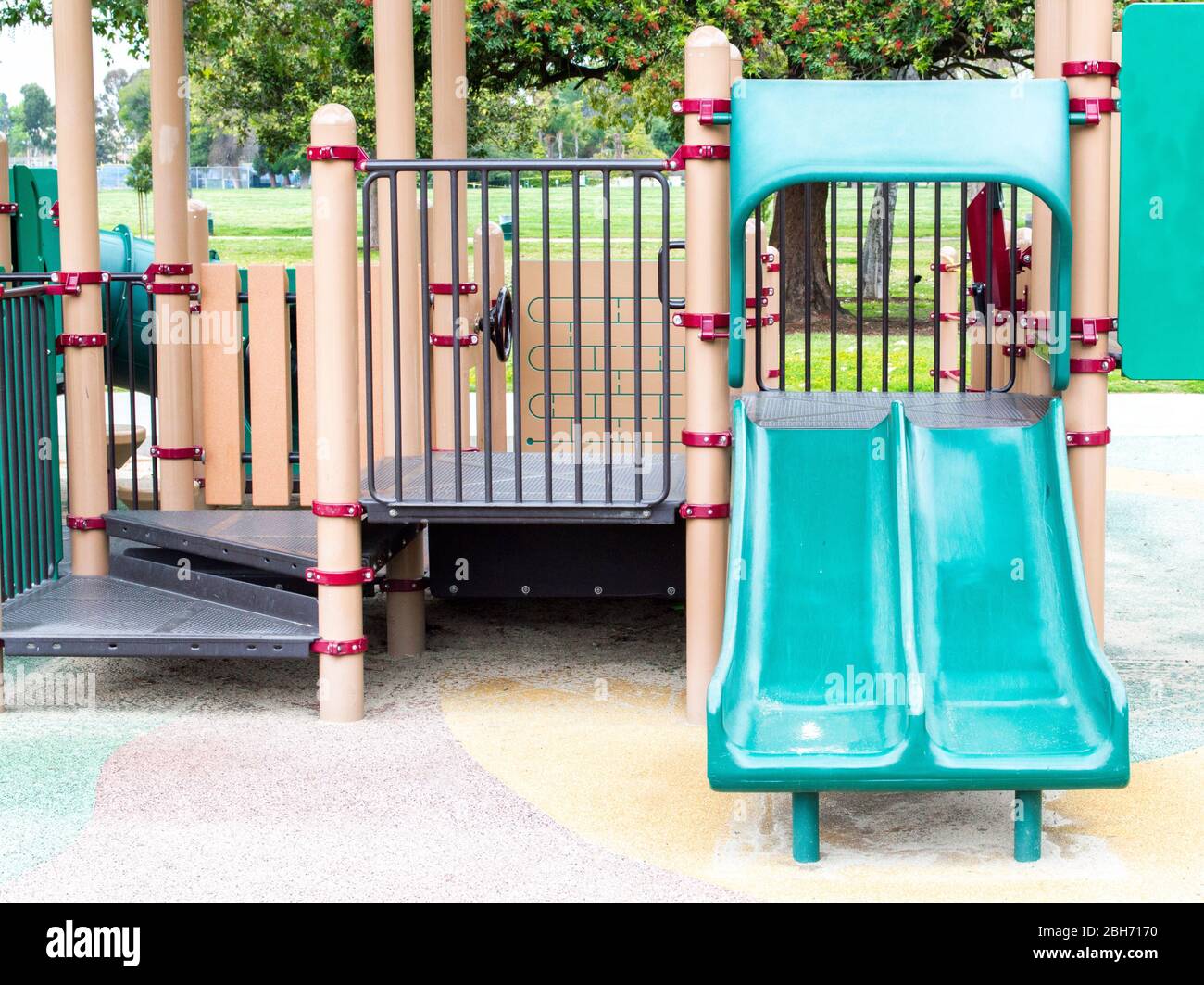 an empty green double slide with metal steps at a colorful outdoor ...
