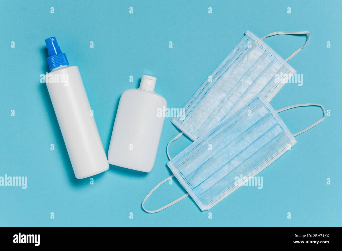 Coronavirus protection. Medical surgical masks and bottles of disinfectant and alcohol hand sanitizer on blue background. Hygiene measures to prevent Stock Photo