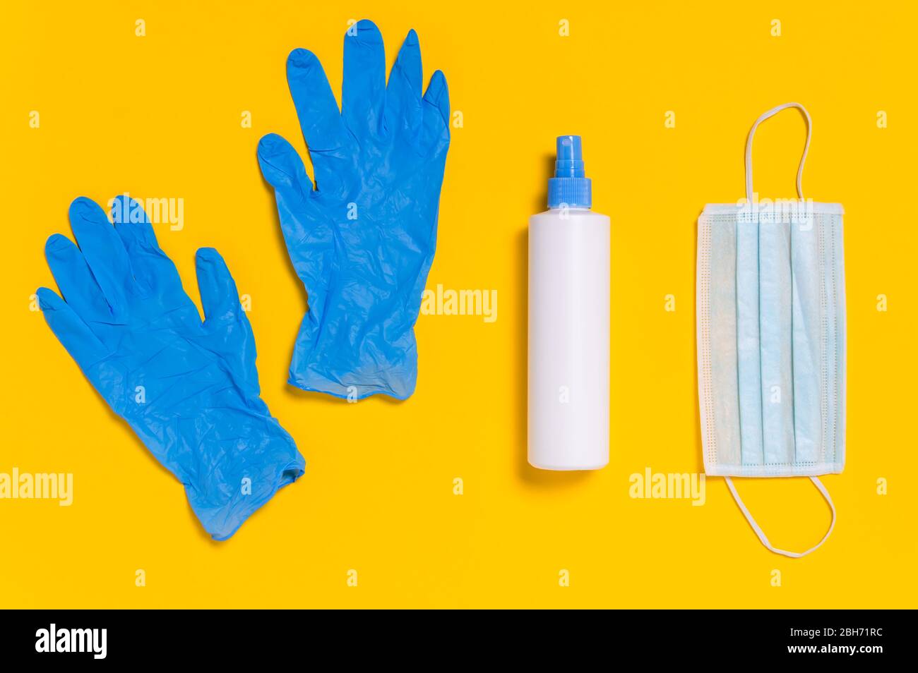 Coronavirus protection. Medical surgical mask, disinfectant or hand sanitizer and blue disposable gloves on yellow background. Hygiene measures to pre Stock Photo