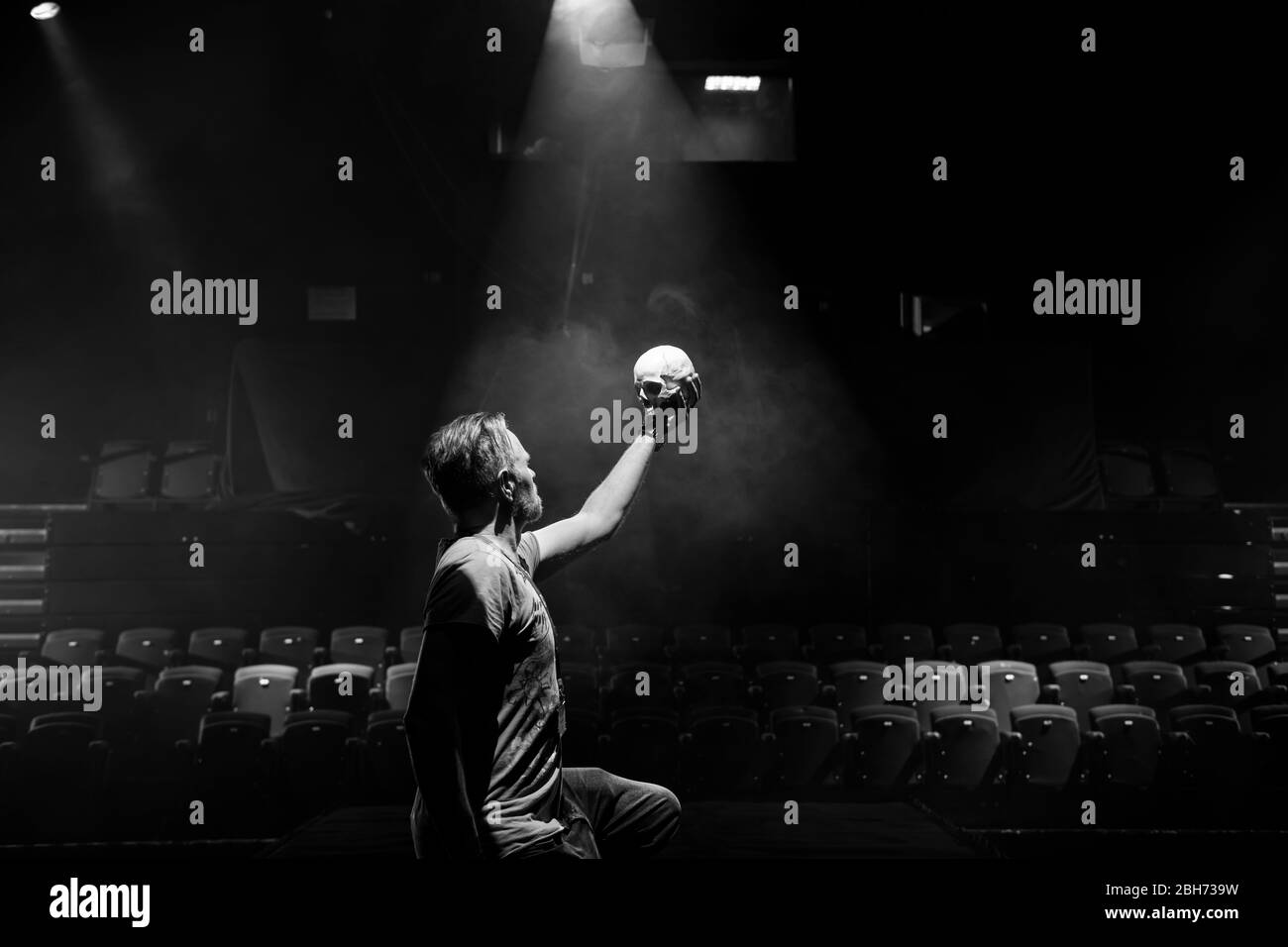 Actor on stage performing Hamlet yorik scene with skull, black and white with spotlight Stock Photo
