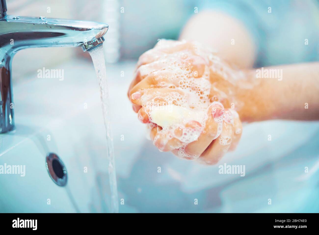 A man carefully washes his hands with soap and thick foam in the bathroom over the sink, from the tap of which water flows. Stock Photo
