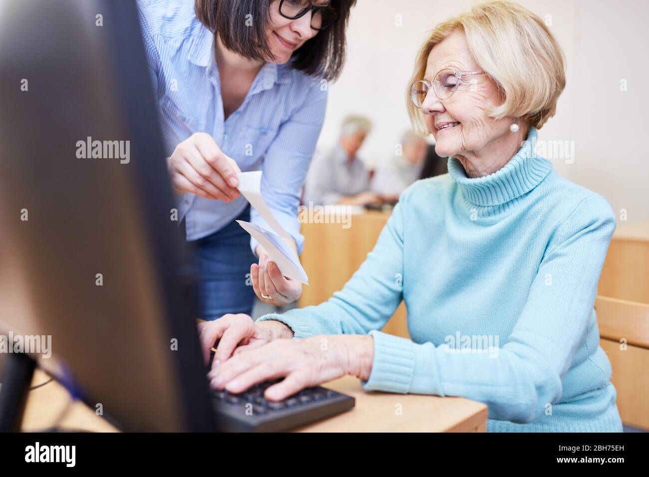 VHS lecturer helps senior citizen on PC in computer course with
