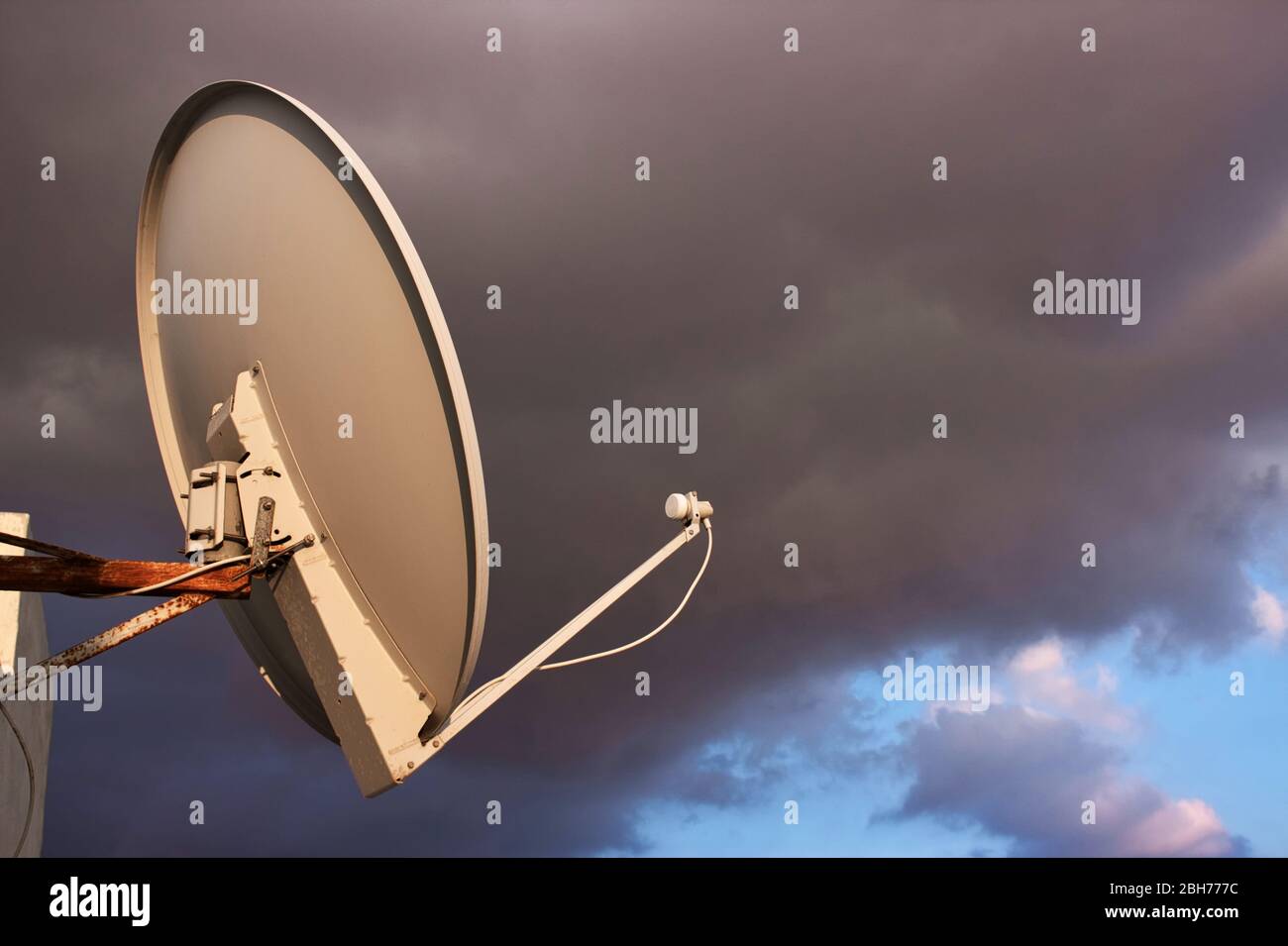Satellite dish on a rooftop against a cloudy moody sky background Stock Photo